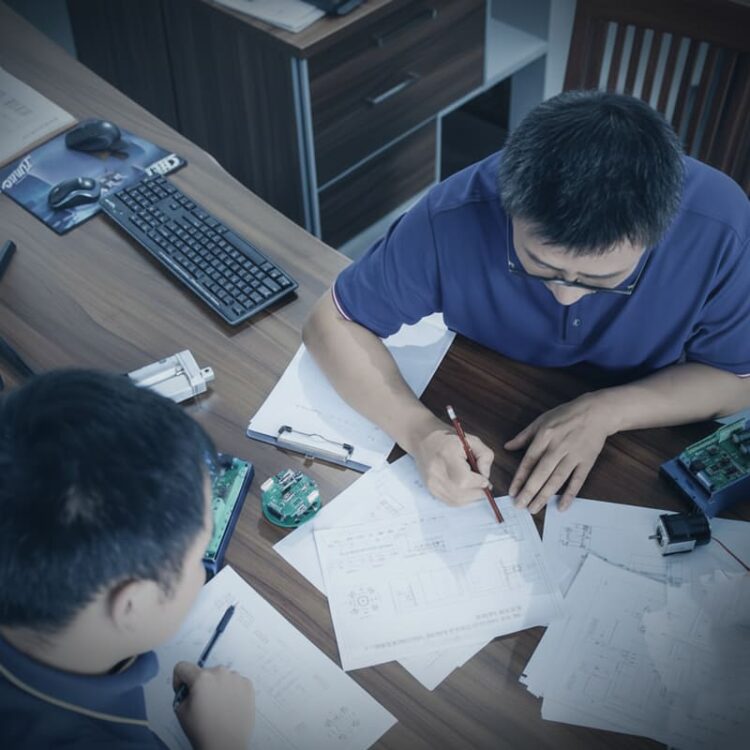 Team of engineers collaborating over custom BLDC motor blueprints and PCB components, illustrating the requirements evaluation and design process.